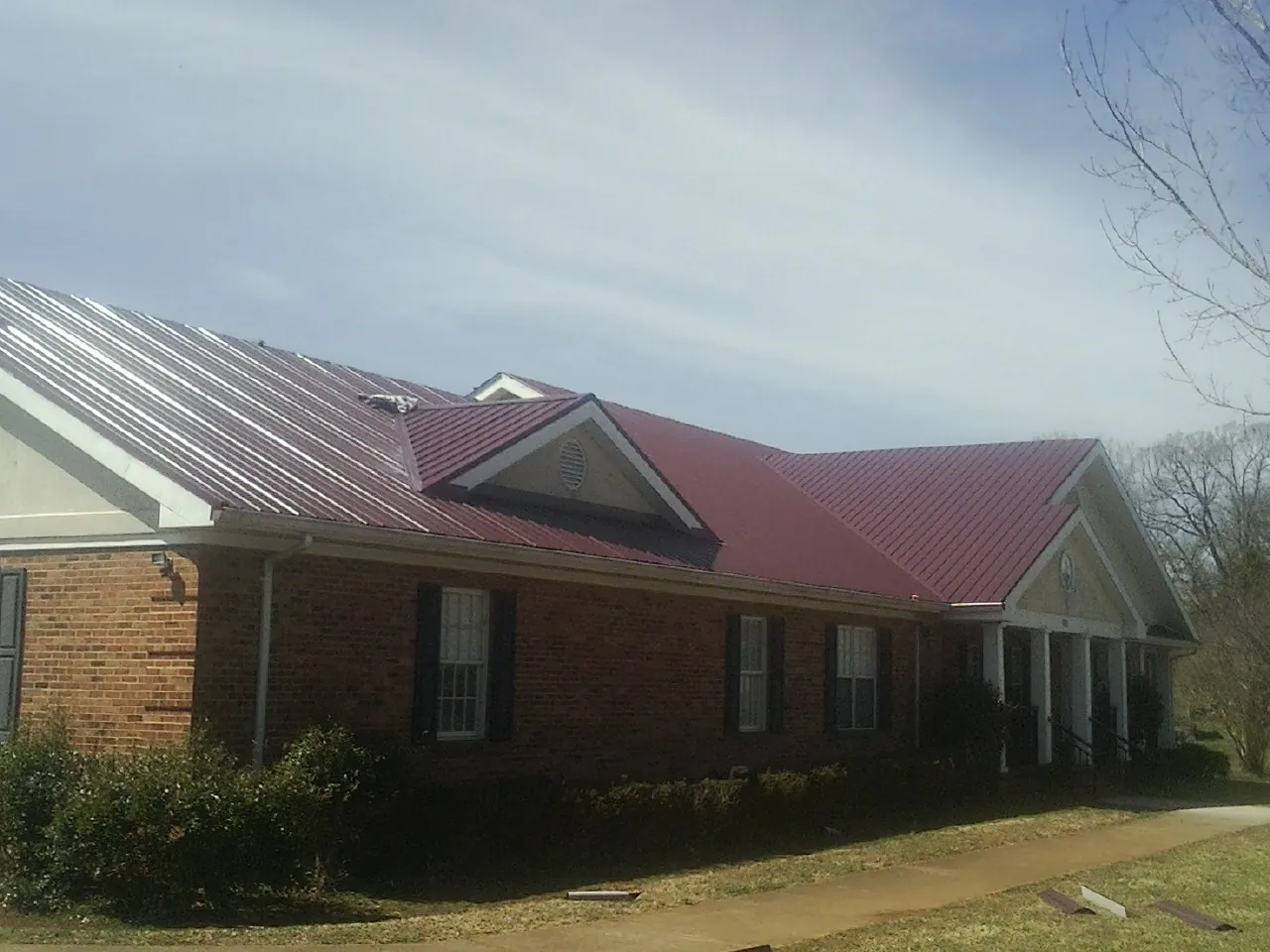 Red metal roof with gabled entries on a long brick building, from a Hail Damage Roof Repair job in Mathews