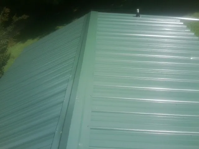 New green metal panels meeting at the ridge of a roof — Flat Roof Repair work by our crew in Mathews